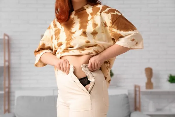 Image of woman trying to do her trousers up after pregnancy weight gain Calne